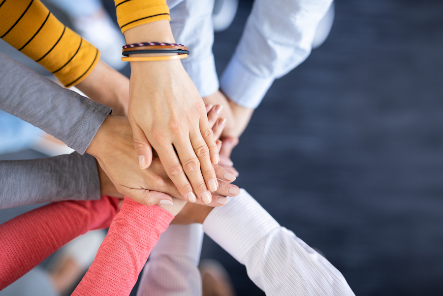 Une vue d'en haut en gros plan d'une équipe superposant ses mains au centre pour symboliser la solidarité, l'unité et le travail d'équipe.